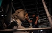 A craftsman meticulously works on a large clay sculpture of a deity inside a dimly lit workshop. The sculpture has intricate details, including flowing hair and a serene facial expression. Wooden scaffolding surrounds the scene, and the craftsman uses a cloth to smooth the surface.