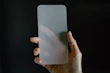 A hand holding a tempered glass screen protector ready to be installed on an iPhone.