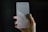 A hand is holding a frosted glass screen protector against a dark background. The glass has rounded corners and appears translucent, partially obscuring the hand behind it.