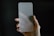 A hand is holding a frosted glass screen protector against a dark background. The glass has rounded corners and appears translucent, partially obscuring the hand behind it.
