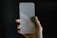 A hand is holding a frosted glass screen protector against a dark background. The glass has rounded corners and appears translucent, partially obscuring the hand behind it.