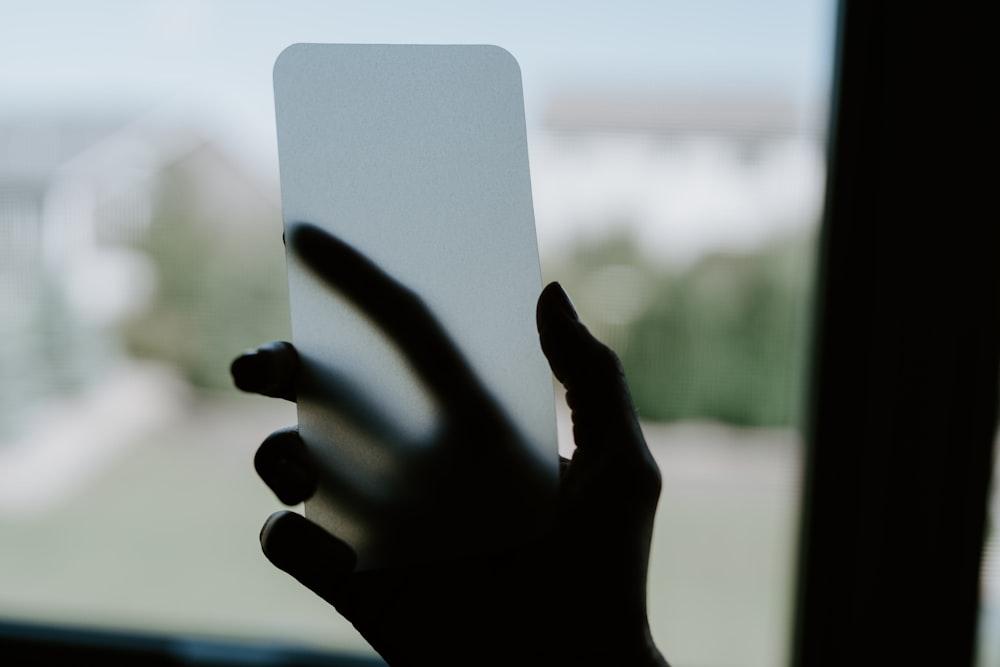 a hand holding a white card in front of a window