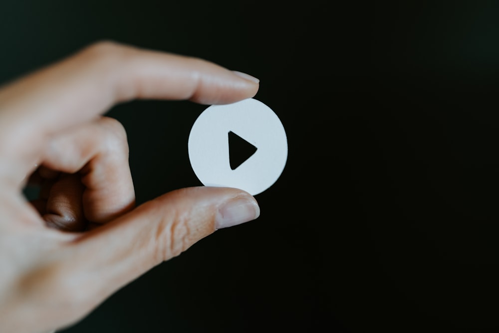 a hand holding a white paper cut out of a video play button