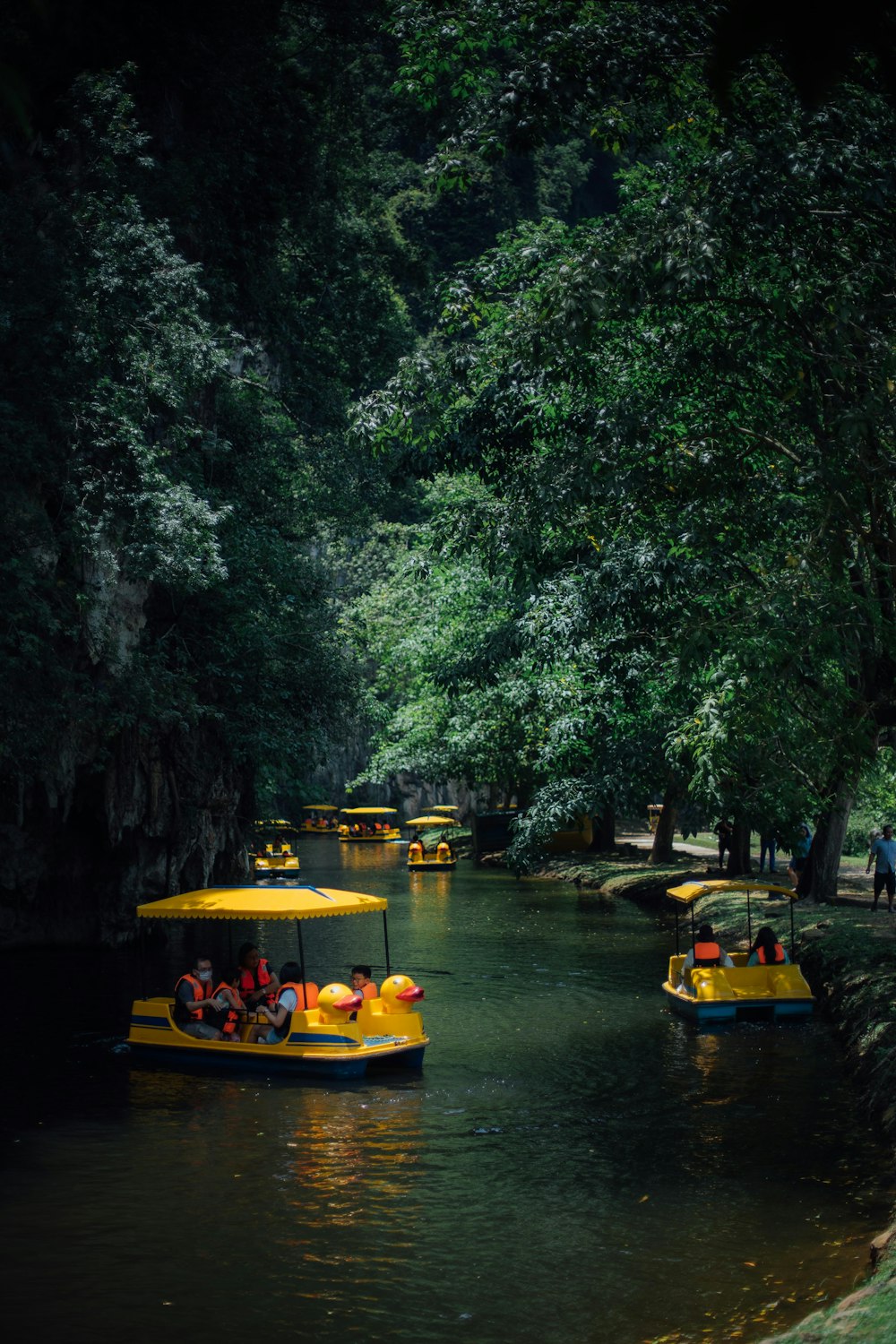 a group of yellow boats floating down a river next to a lush green forest