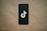 A black smartphone is placed on a beige background with a TikTok logo prominently displayed on the screen.