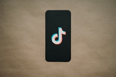 A black smartphone is placed on a beige background with a TikTok logo prominently displayed on the screen.