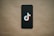 A black smartphone is placed on a beige background with a TikTok logo prominently displayed on the screen.