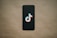 A black smartphone is placed on a beige background with a TikTok logo prominently displayed on the screen.