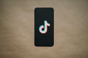 A black smartphone is placed on a beige background with a TikTok logo prominently displayed on the screen.