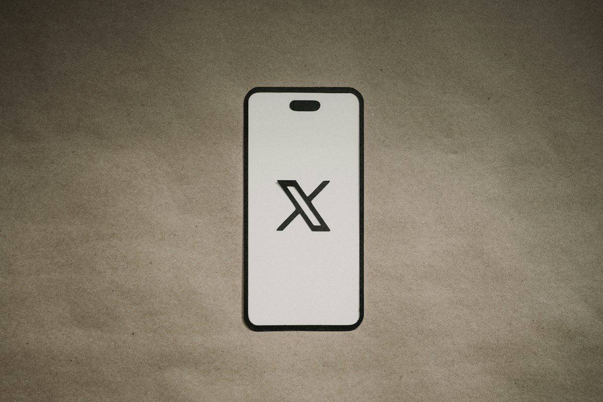 The X logo on a paper cut-out shaped like a phone, standing for the official X app.