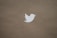 A white silhouette of a bird is centered on a plain brown cardboard background. The bird is rendered in a minimalistic style, likely representing a logo.