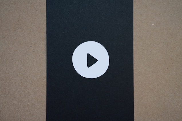 A simple circular play button icon is centered on a black vertical strip that contrasts with the surrounding brownish-beige background.