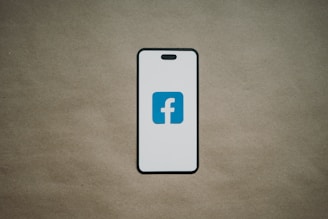 A smartphone is depicted with a white screen displaying a blue logo with the letter 'f', set against a plain brown background.