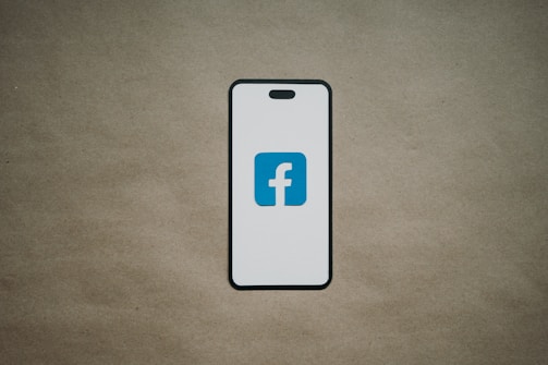 A smartphone is depicted with a white screen displaying a blue logo with the letter 'f', set against a plain brown background.