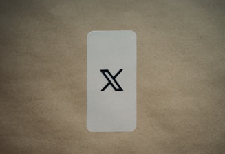 A simple, vertically aligned rectangular card with rounded corners placed on a textured brown surface. In the center of the card, there's a large black stylized 'X' symbol. The background is a plain, light brown color which contrasts with the card's lighter shade.