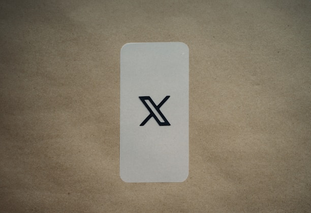 A simple, vertically aligned rectangular card with rounded corners placed on a textured brown surface. In the center of the card, there's a large black stylized 'X' symbol. The background is a plain, light brown color which contrasts with the card's lighter shade.