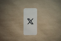 A simple, vertically aligned rectangular card with rounded corners placed on a textured brown surface. In the center of the card, there's a large black stylized 'X' symbol. The background is a plain, light brown color which contrasts with the card's lighter shade.