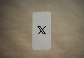 A simple, vertically aligned rectangular card with rounded corners placed on a textured brown surface. In the center of the card, there's a large black stylized 'X' symbol. The background is a plain, light brown color which contrasts with the card's lighter shade.