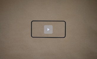 A blank brown background with a black rectangle outline in the center. Inside the outline, there is a light gray play button icon.