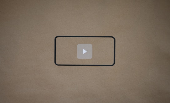 A blank brown background with a black rectangle outline in the center. Inside the outline, there is a light gray play button icon.
