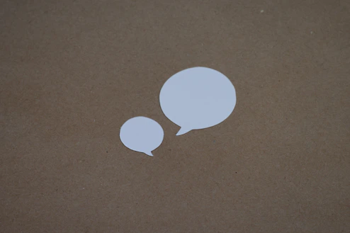 two white speech bubbles sitting on top of a brown surface