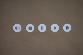 Five circular white icons on a brown background, each representing sound and playback controls. These include a speaker, stop, pause, play, and fast-forward symbol.