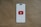 A smartphone-like rectangular shape is centered on a brown textured background. The shape has a white screen with rounded edges and features a prominent red play button inside a white triangle in the center, resembling the YouTube logo.
