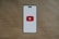 A smartphone-like rectangular shape is centered on a brown textured background. The shape has a white screen with rounded edges and features a prominent red play button inside a white triangle in the center, resembling the YouTube logo.