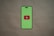 A smartphone silhouette with a bright green screen displays a red play button symbol in the center, resembling the YouTube logo. The background is a plain, neutral brown surface.