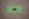A green card with rounded corners features a prominent red play button symbol in the center, set against a plain brown textured background.
