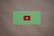 A green card with rounded corners features a prominent red play button symbol in the center, set against a plain brown textured background.
