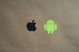 Two logos are positioned on a plain brown background. The black apple logo is on the left side, and the green android robot logo is on the right.