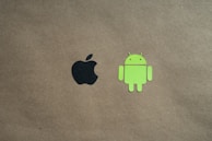 Two logos are positioned on a plain brown background. The black apple logo is on the left side, and the green android robot logo is on the right.