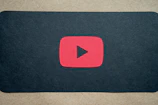 A minimalist YouTube play button illuminated in gold on a dark backdrop.