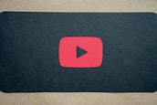 A red play button symbol is centered on a dark background, resembling the YouTube logo.