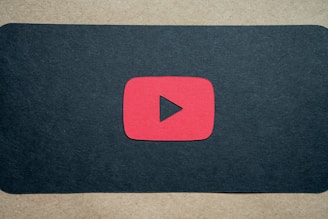 A red play button symbol is centered on a dark background, resembling the YouTube logo.