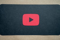 A red play button symbol is centered on a dark background, resembling the YouTube logo.