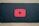 A red play button symbol is centered on a dark background, resembling the YouTube logo.