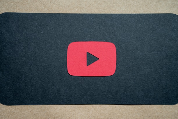 A red play button symbol is centered on a dark background, resembling the YouTube logo.