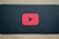A red play button symbol is centered on a dark background, resembling the YouTube logo.