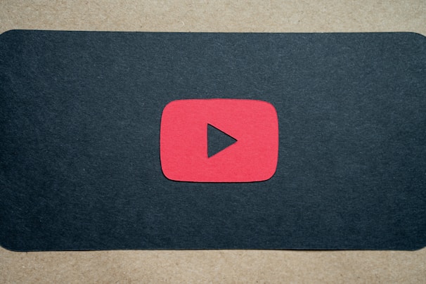 A red play button symbol is centered on a dark background, resembling the YouTube logo.