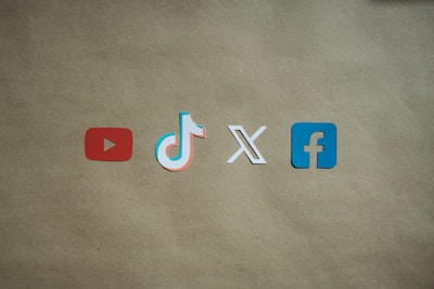 Four social media platform logos are arranged on a brown background. From left to right, the logos are for YouTube in red, TikTok in a combination of red, blue, and white, X in white, and Facebook in blue.