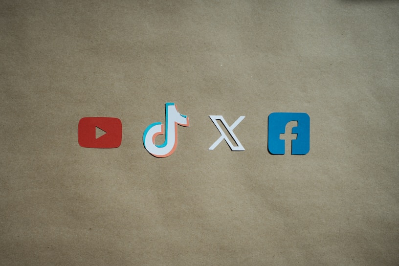 Four social media platform logos are arranged on a brown background. From left to right, the logos are for YouTube in red, TikTok in a combination of red, blue, and white, X in white, and Facebook in blue.