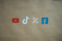 Four social media platform logos are arranged on a brown background. From left to right, the logos are for YouTube in red, TikTok in a combination of red, blue, and white, X in white, and Facebook in blue.