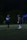 Two football players in blue jerseys are standing on a dimly lit football field. One player is wearing the number 24. There is a blue tent with text and some other individuals in the background.