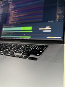 Close-up of hands typing on a laptop keyboard with code on the screen.