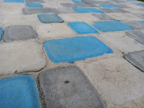 A pattern of square paving stones in a repeating arrangement of blue and gray hues. The stones have rough textures and are set in a slightly worn surface, appearing to form a path or patio.