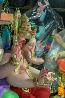 A colorful statue of the Hindu deity Ganesha with elaborate golden adornments and detailed craftsmanship. The statue features vibrant colors and intricate patterns, with a decorated headdress and ornate jewelry.