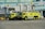 Two large, lime-green airport fire trucks are parked in front of gate 52 at an airport terminal. The vehicles are equipped with fire fighting equipment and have 'R4' markings. The background includes passenger boarding bridges, airport signage and the HSBC logo on a building facade.