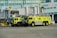 Two large, lime-green airport fire trucks are parked in front of gate 52 at an airport terminal. The vehicles are equipped with fire fighting equipment and have 'R4' markings. The background includes passenger boarding bridges, airport signage and the HSBC logo on a building facade.